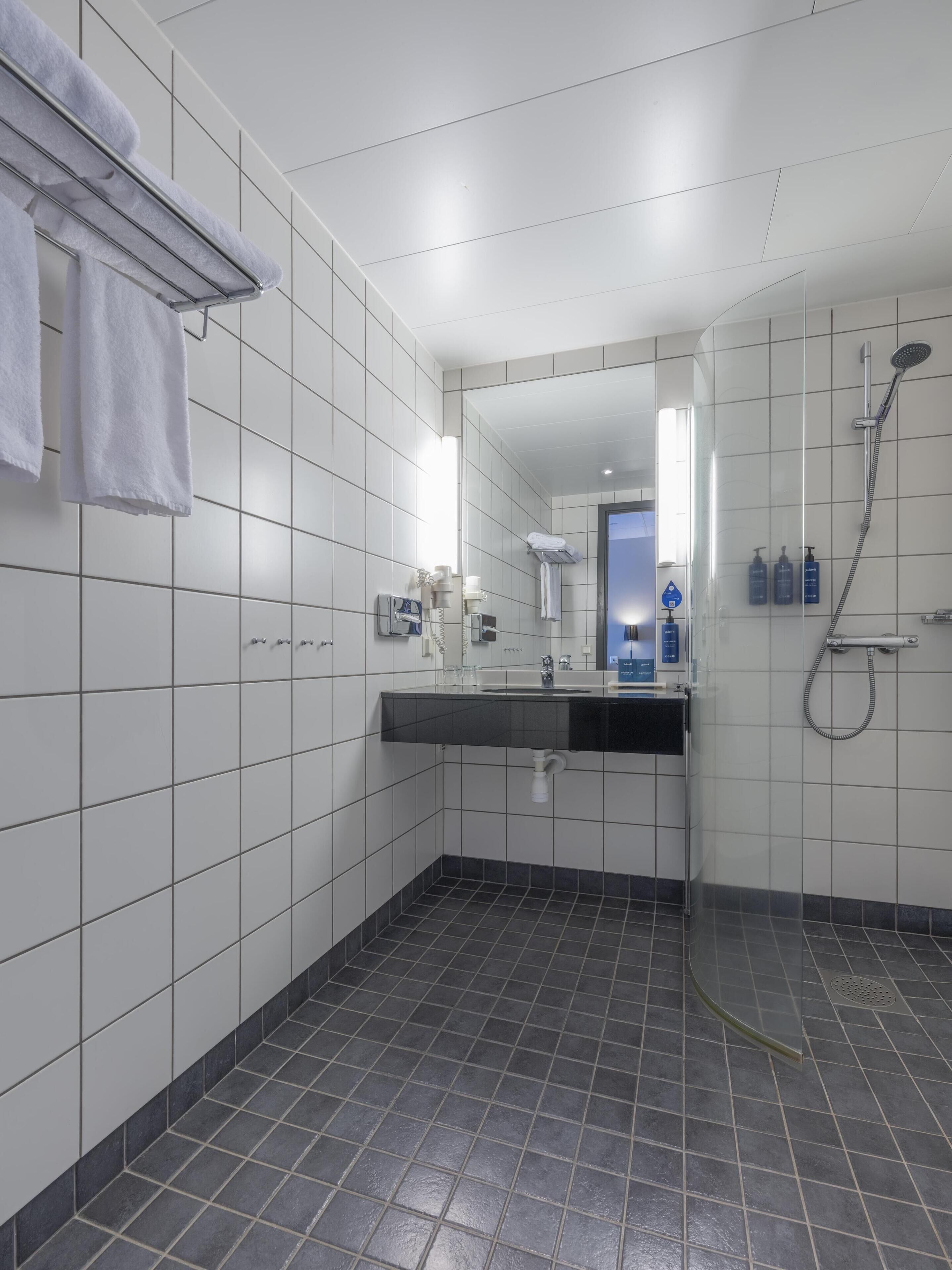 A modern bathroom with white tiled walls, a black countertop, a glass shower enclosure, and a visible sink.