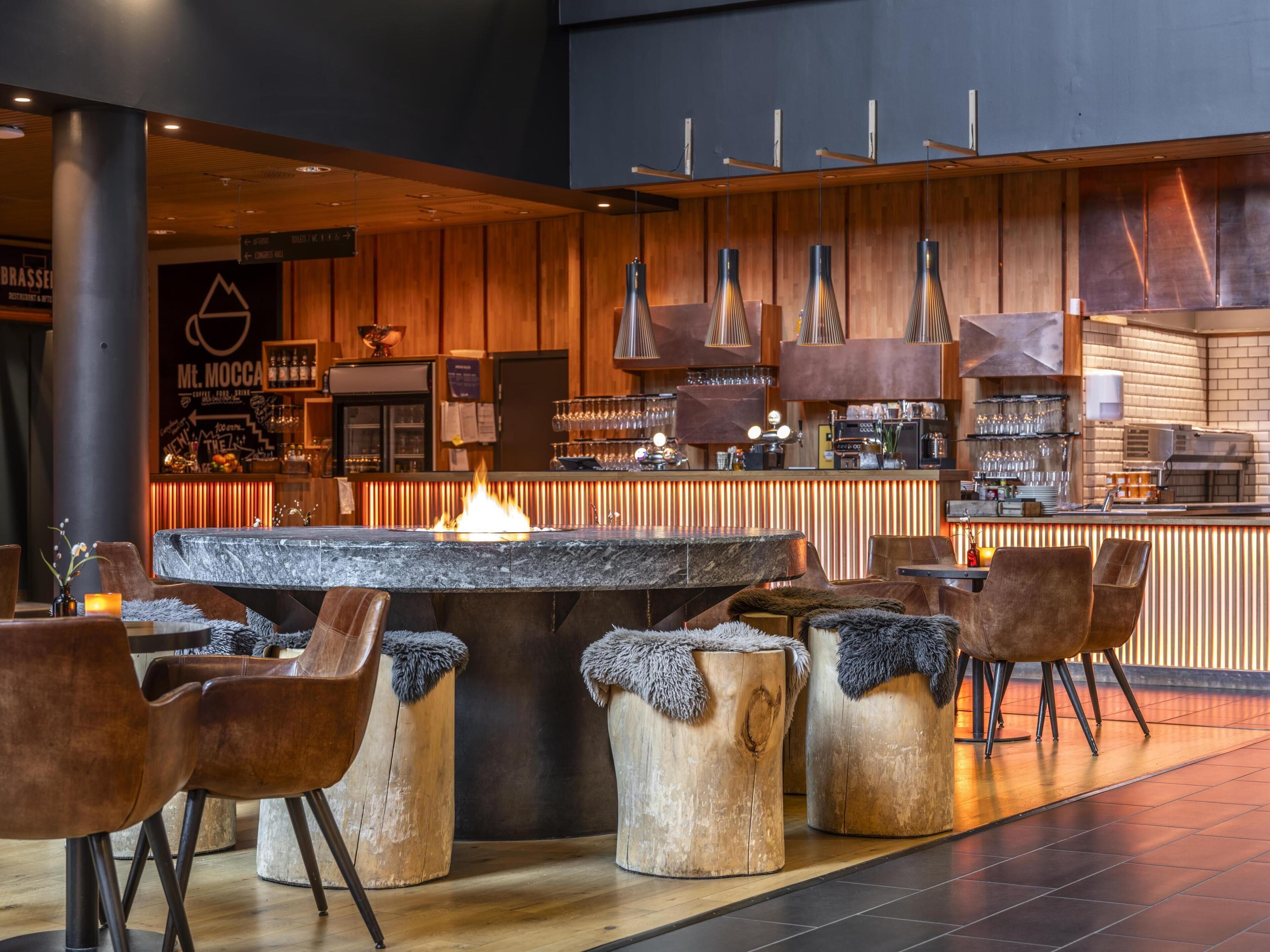 Een moderne bar met een open haard in het midden, houten krukken en een bargedeelte.