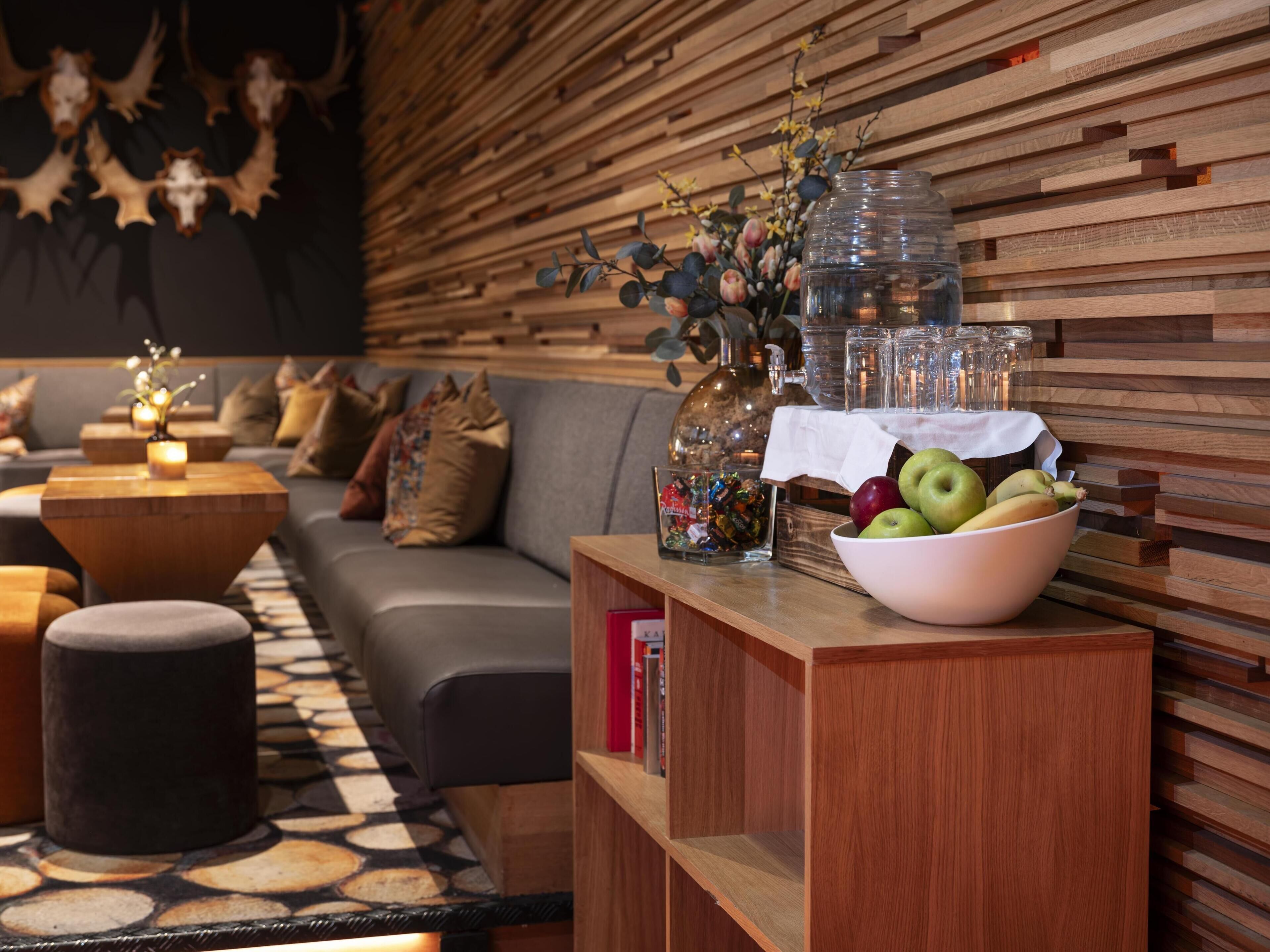 A modern living room with a wooden wall, a grey sofa, a wooden coffee table, and a bowl of fruit on a wooden side table.