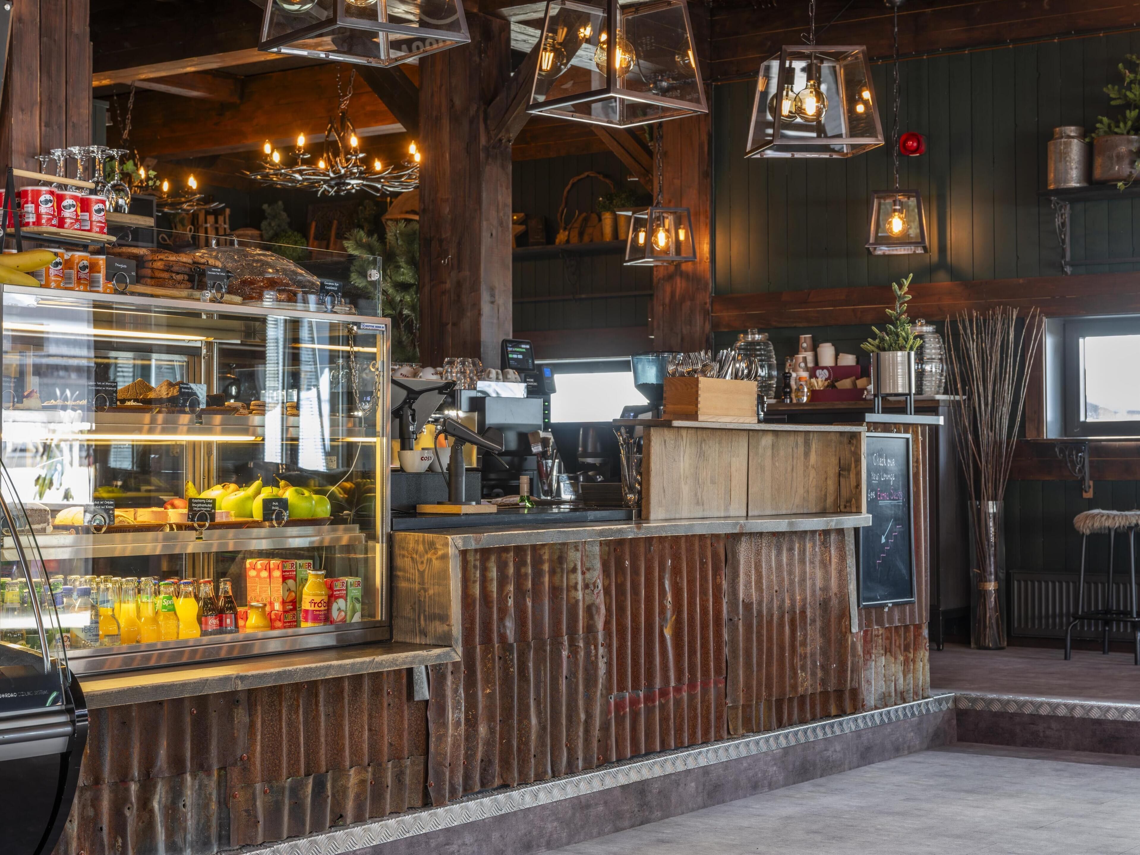 A rustic cafe interior with a wooden counter, a glass display case with pastries, and hanging pendant lights.