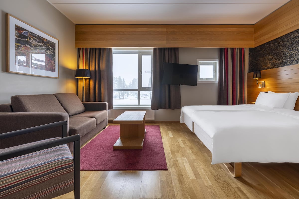 A hotel room with a sofa, a bed, a TV, and a window with curtains.