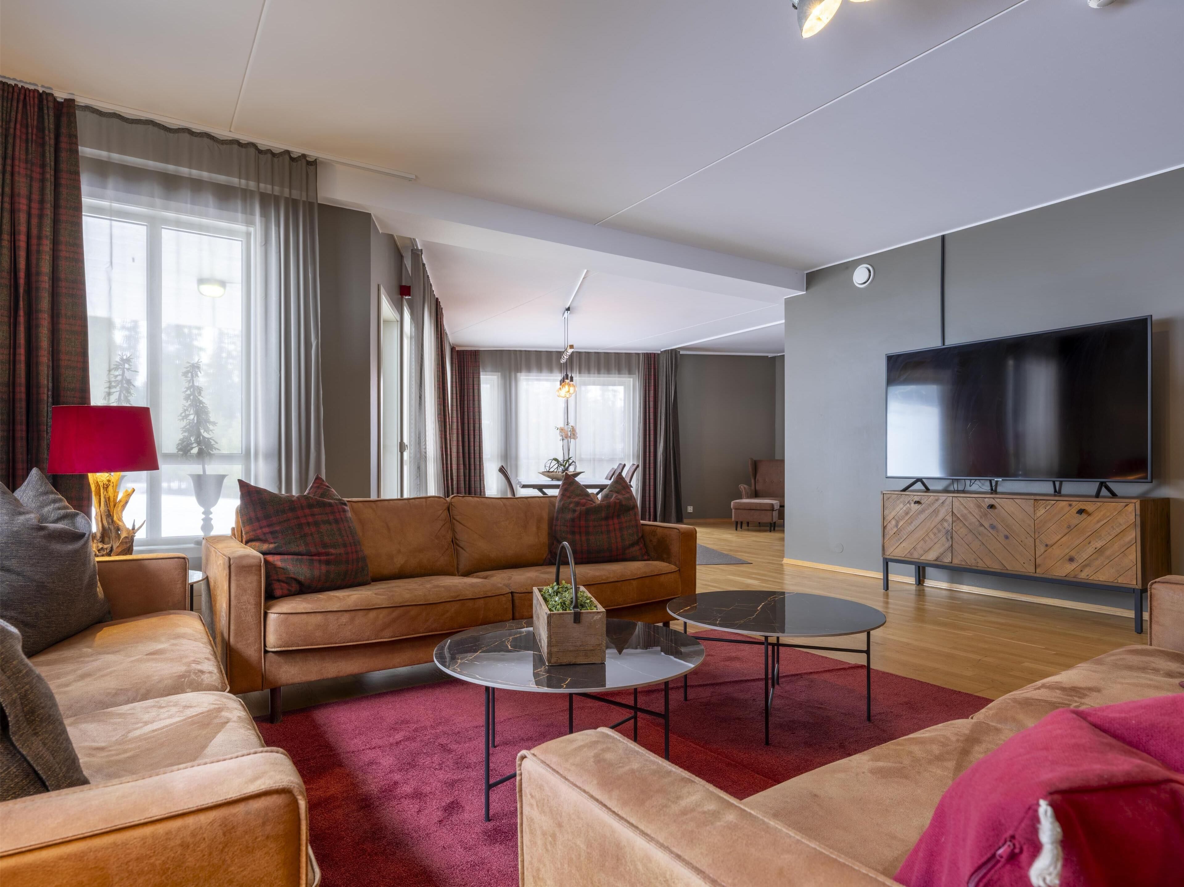 Ein modernes Wohnzimmer mit einer Couch, zwei Couchtischen, einem Fernseher und einem Essbereich im Hintergrund.