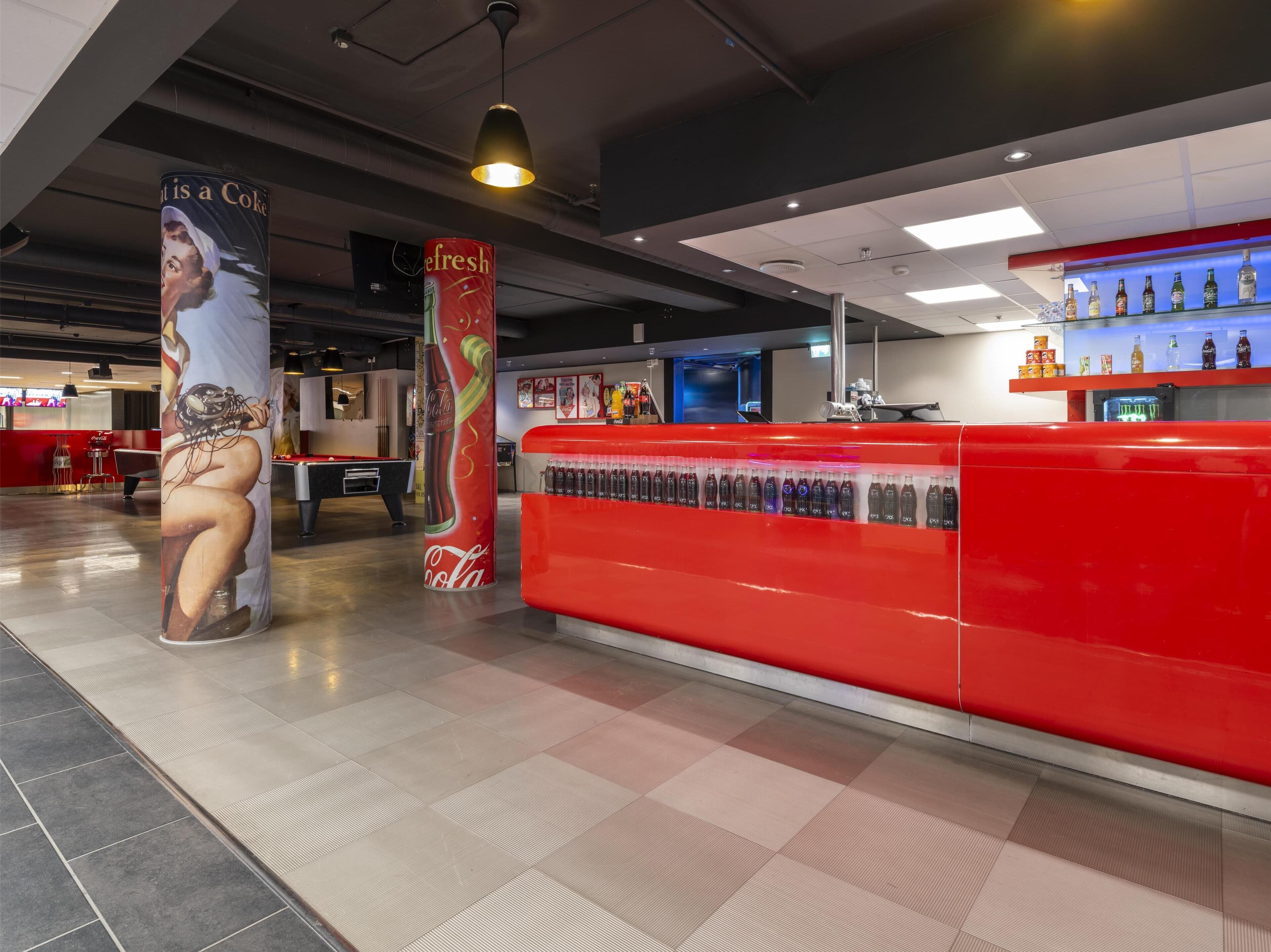 A modern bar area with a red counter, a pool table, and a large Coca-Cola advertisement.