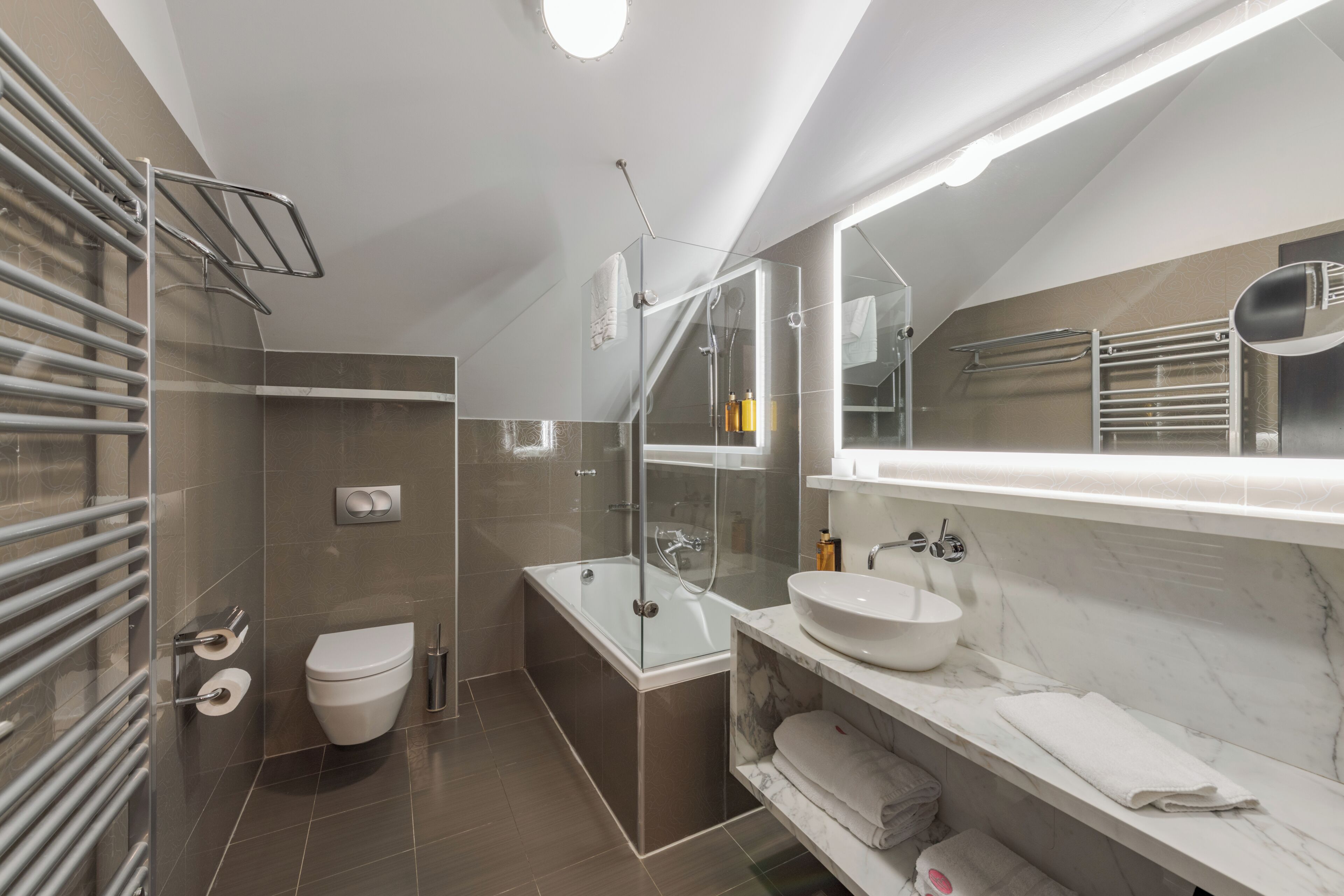 A modern bathroom with a glass-enclosed shower, a white toilet, a built-in sink, and a large mirror.