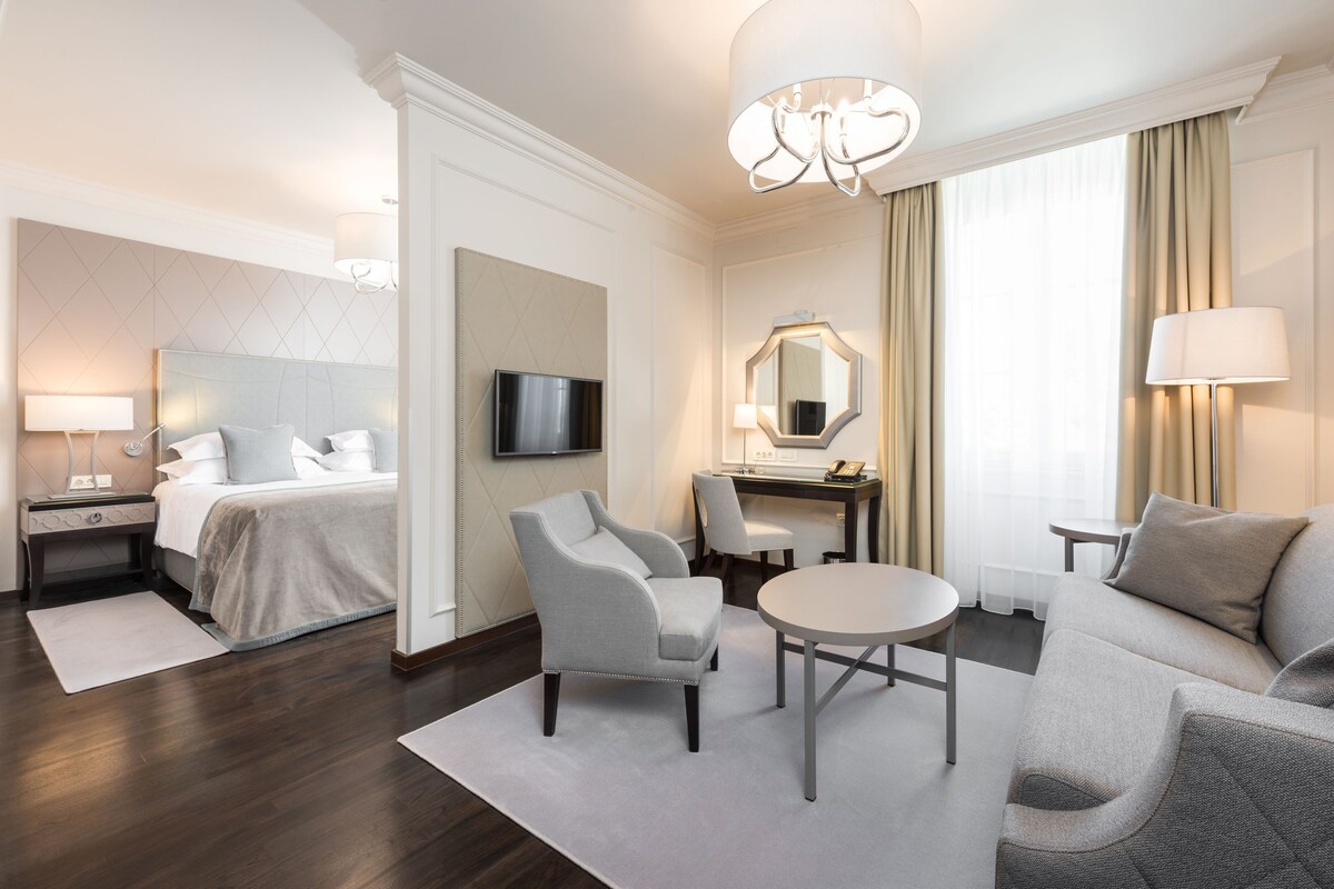 Ein Hotelzimmer mit einem Bett, einem Schreibtisch mit Stuhl, einem Sofa, einem runden Tisch und einem Fernseher.