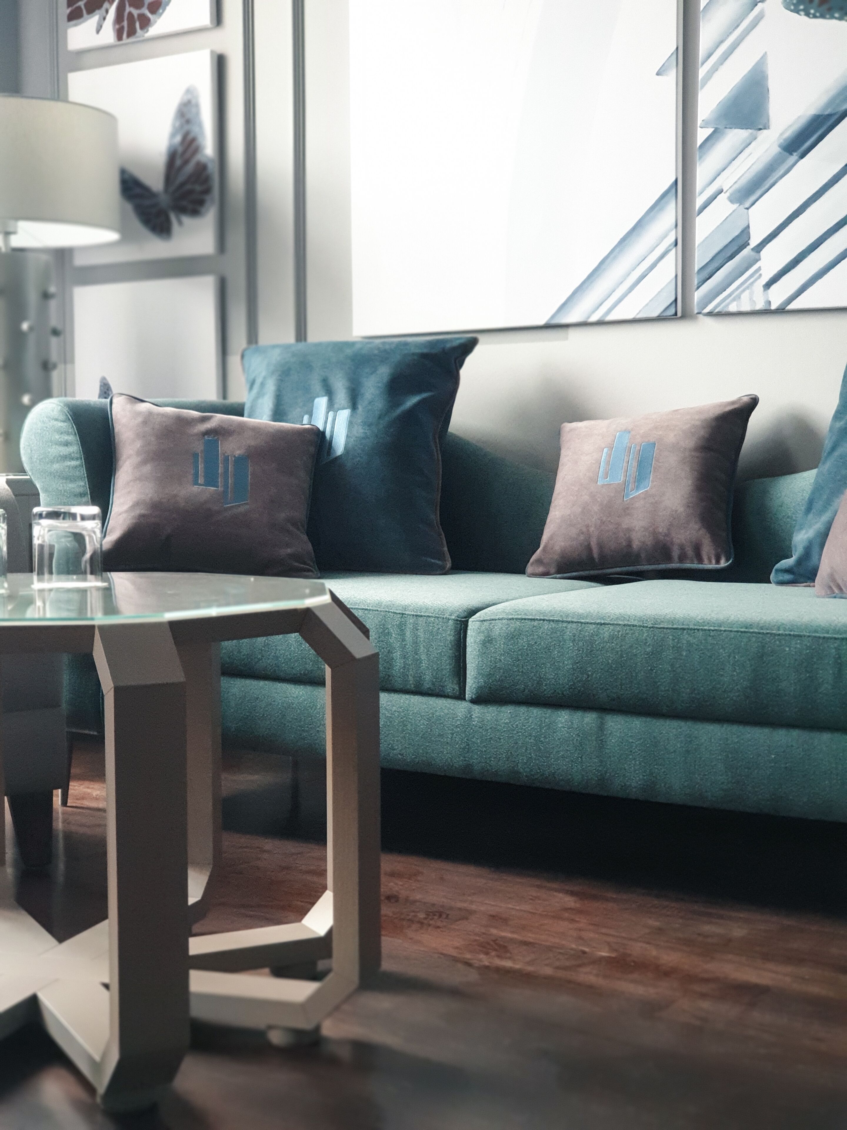 Un salon moderne avec un canapé de couleur turquoise, des coussins à motifs géométriques, une table basse en verre et un plancher en bois.