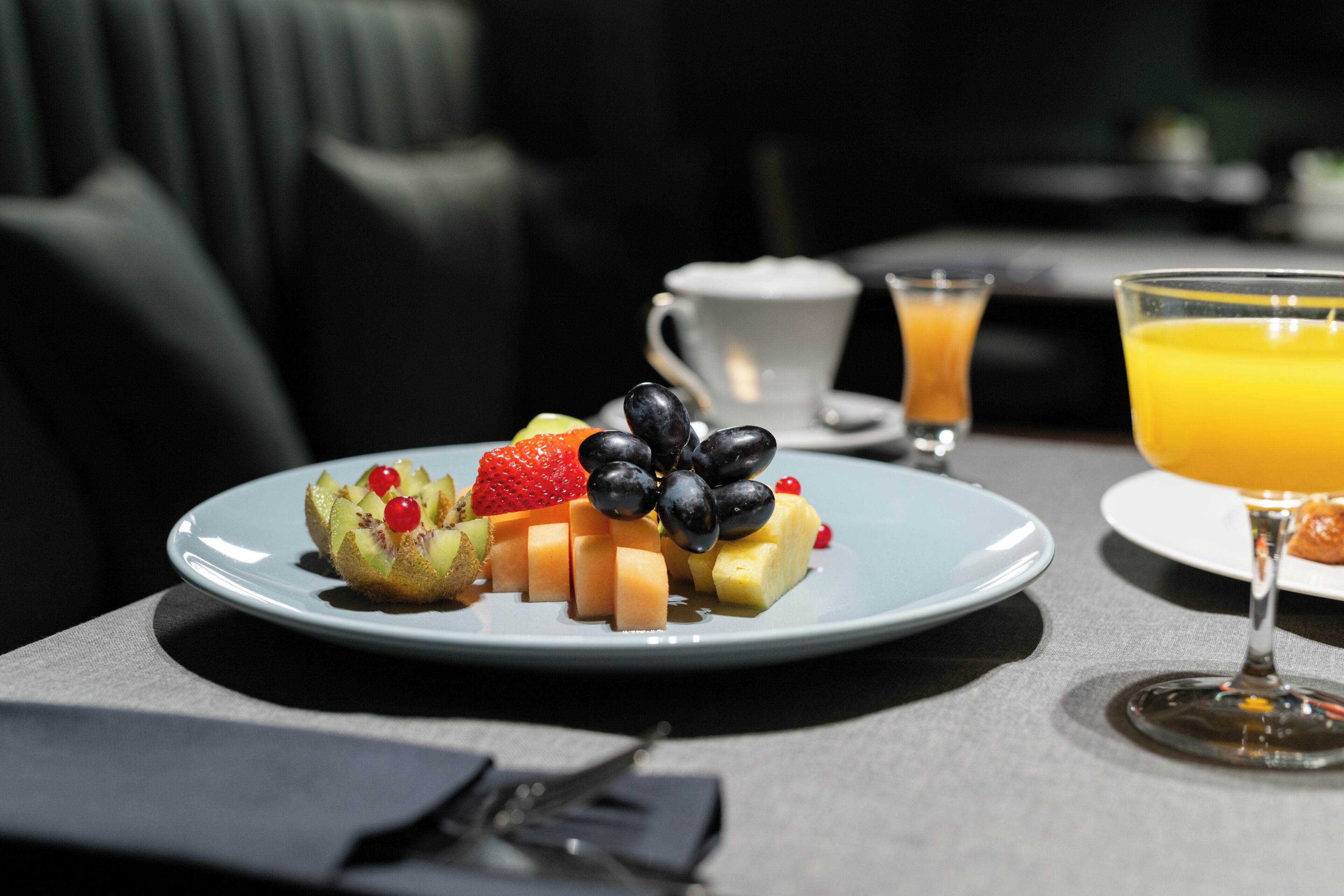 A breakfast setting with a plate of fruit, a cup of coffee, and a glass of orange juice on a table.