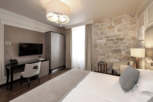 Una habitación de hotel con cama, escritorio, silla, televisor, lámpara y pared de piedra.