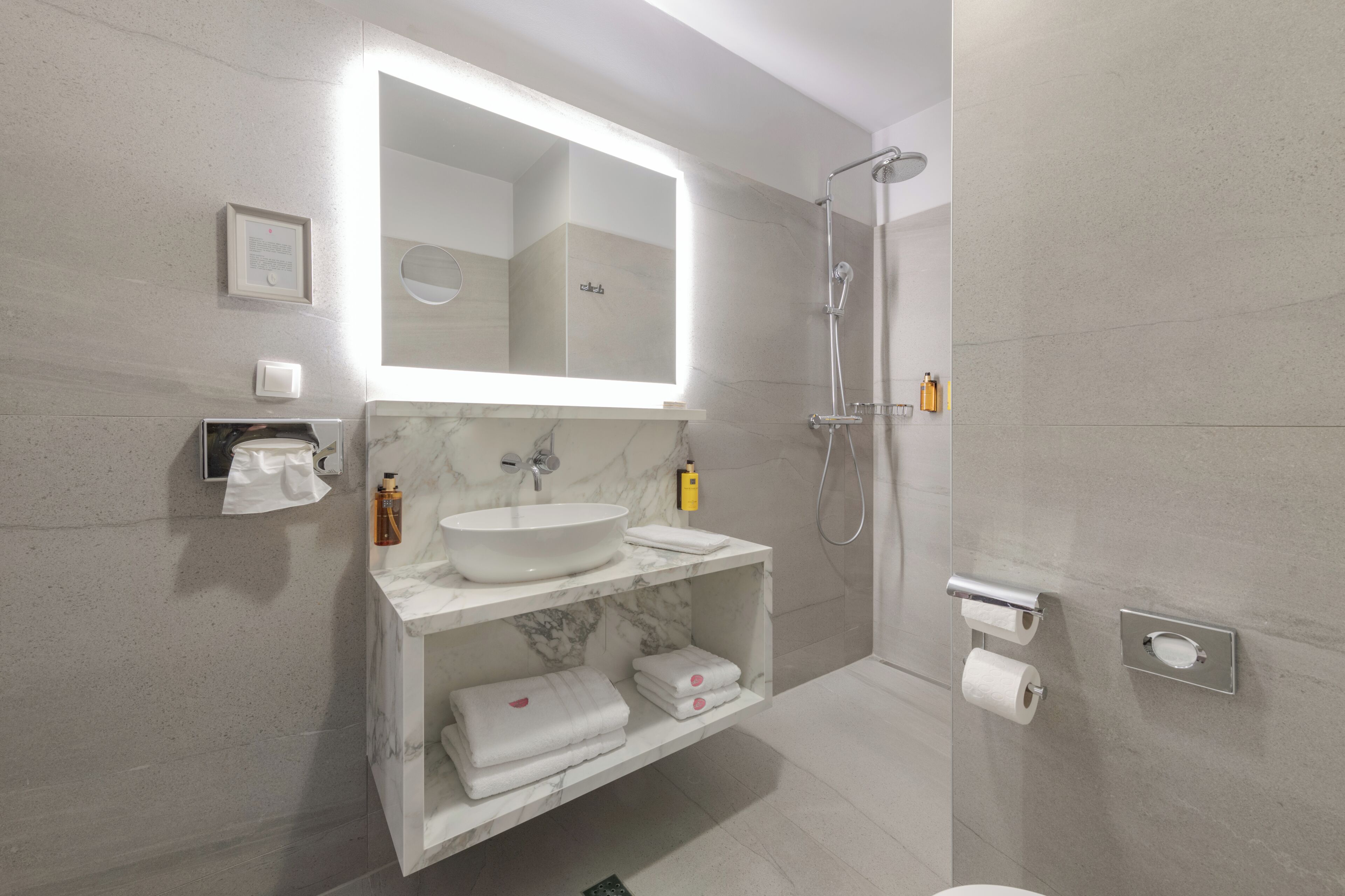 Une salle de bain moderne avec un lavabo en marbre, un grand miroir, une douche et un porte-rouleau de papier toilette.