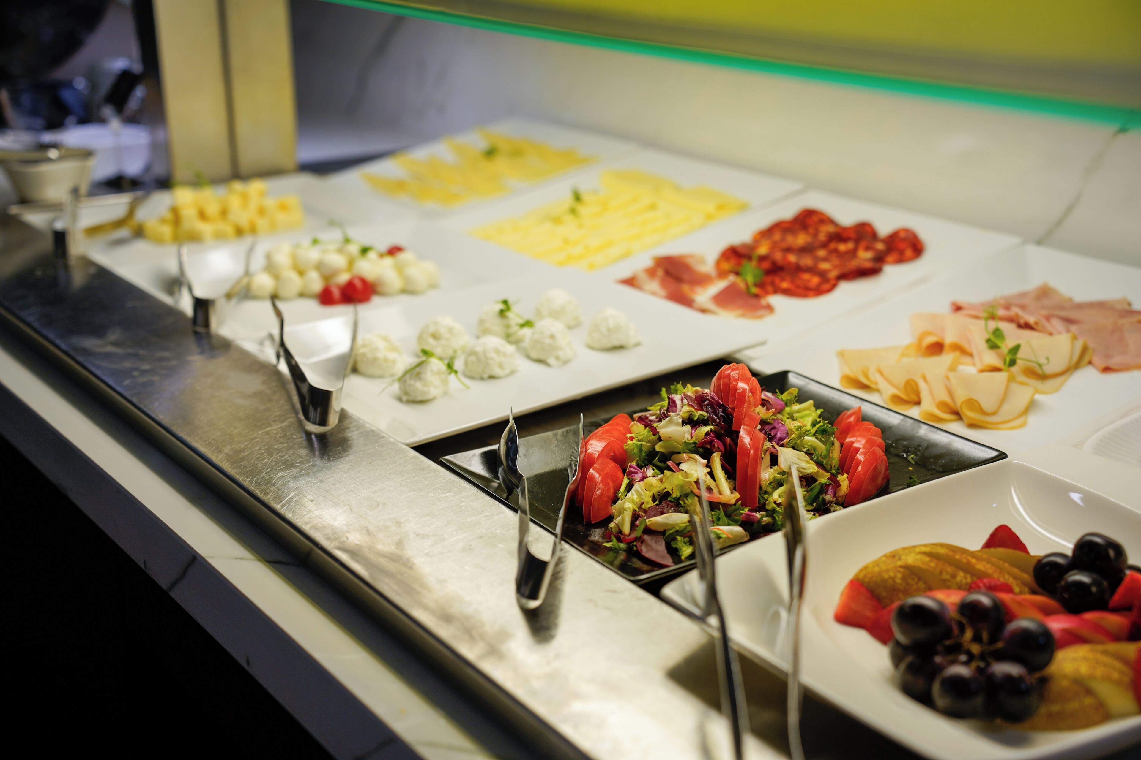 Een buffet met diverse gerechten, waaronder kaas, vleeswaren en fruit.