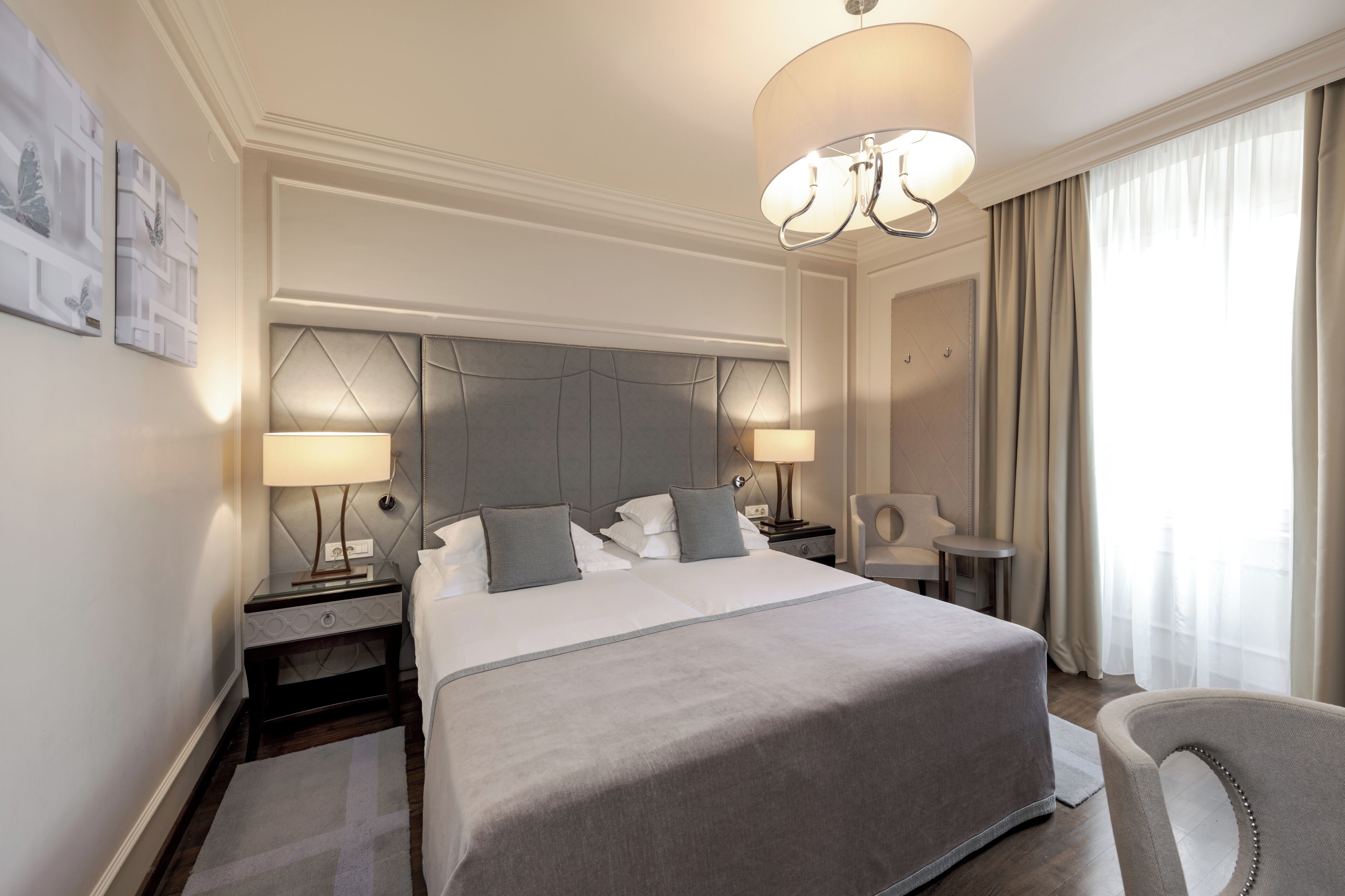 Een hotelkamer met een groot bed, twee nachtkastjes met lampen, een stoel, een bureau en een kroonluchter.