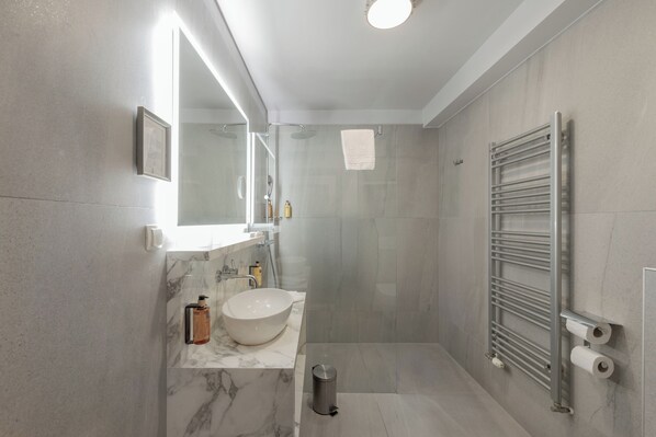 Un baño moderno con lavamanos de mármol, cabina de ducha de vidrio y un perchero para toallas.