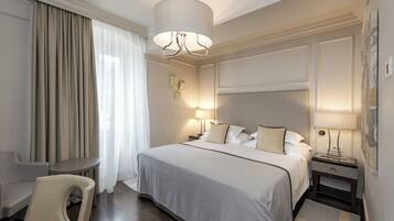 A hotel room with a bed, bedside tables, a chair, a lamp, and a large window with curtains.