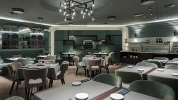 A modern restaurant with round tables, cushioned chairs, and a central light fixture.