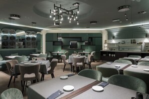 Un restaurante moderno con mesas redondas, sillas acolchadas y una lámpara central.