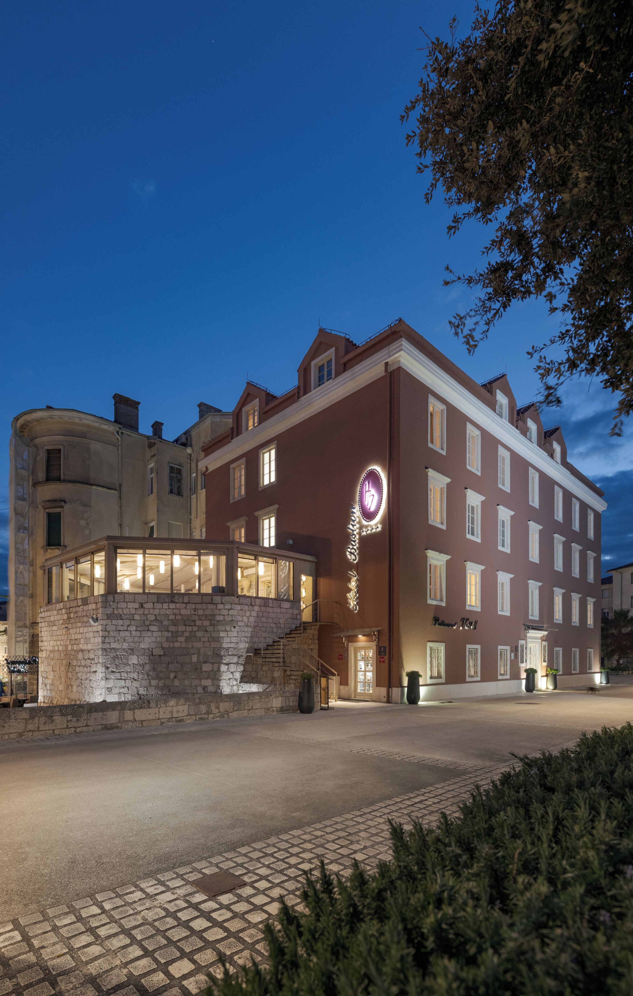 Ein Hotel mit einer steinernen Fassade, zahlreichen Fenstern und einer gut sichtbaren, beleuchteten Beschilderung.