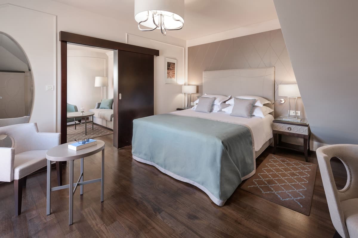Ein modernes Hotelzimmer mit einem großen Bett, einem Schreibtisch, einem Sessel, einem kleinen Tisch und einer separaten Sitzecke mit einer Couch.