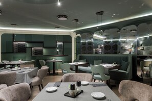 Um restaurante com mesas redondas, assentos acolchoados e iluminação pendente.