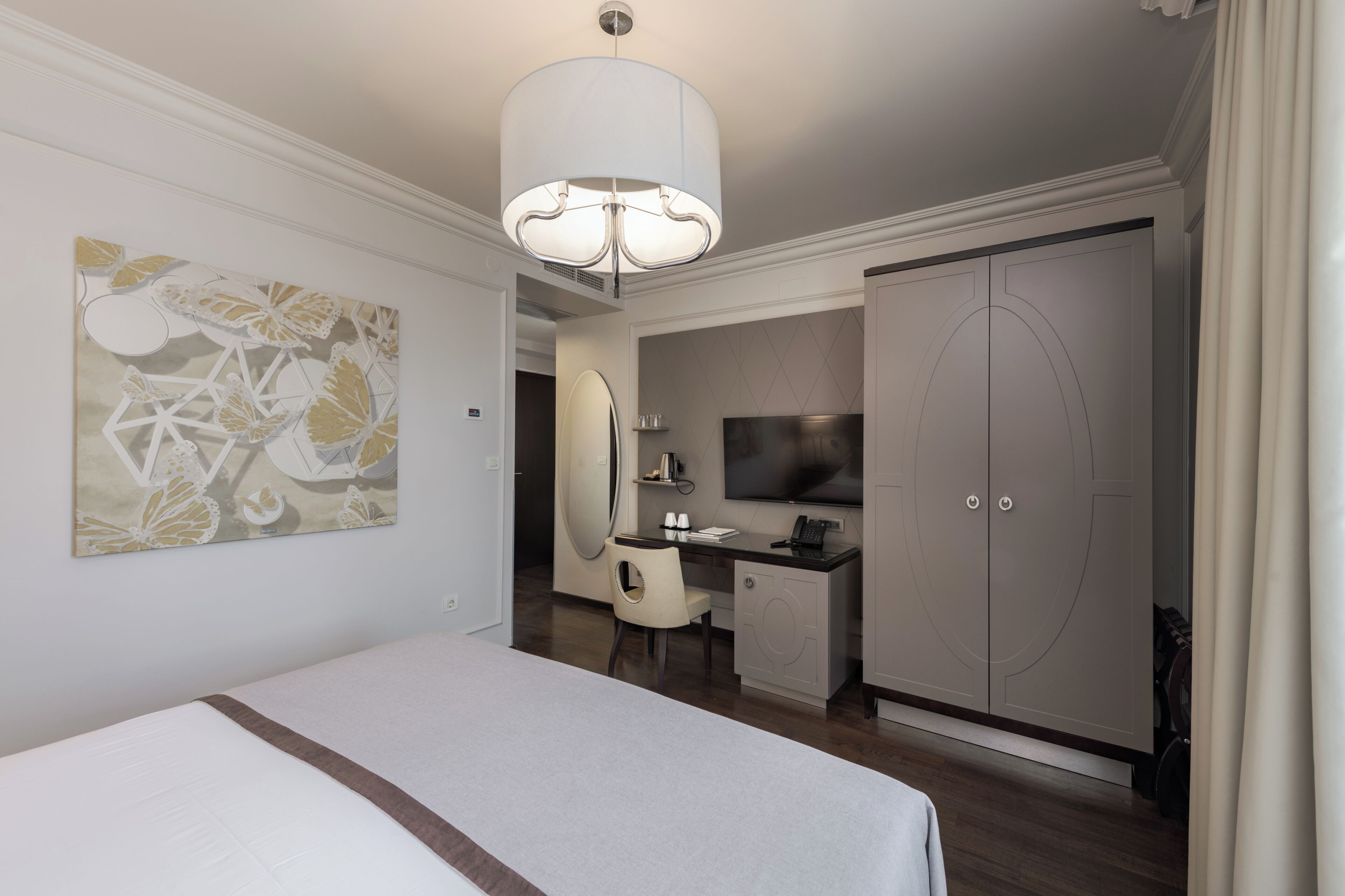 A hotel room with a bed, desk, TV, wardrobe, and artwork.