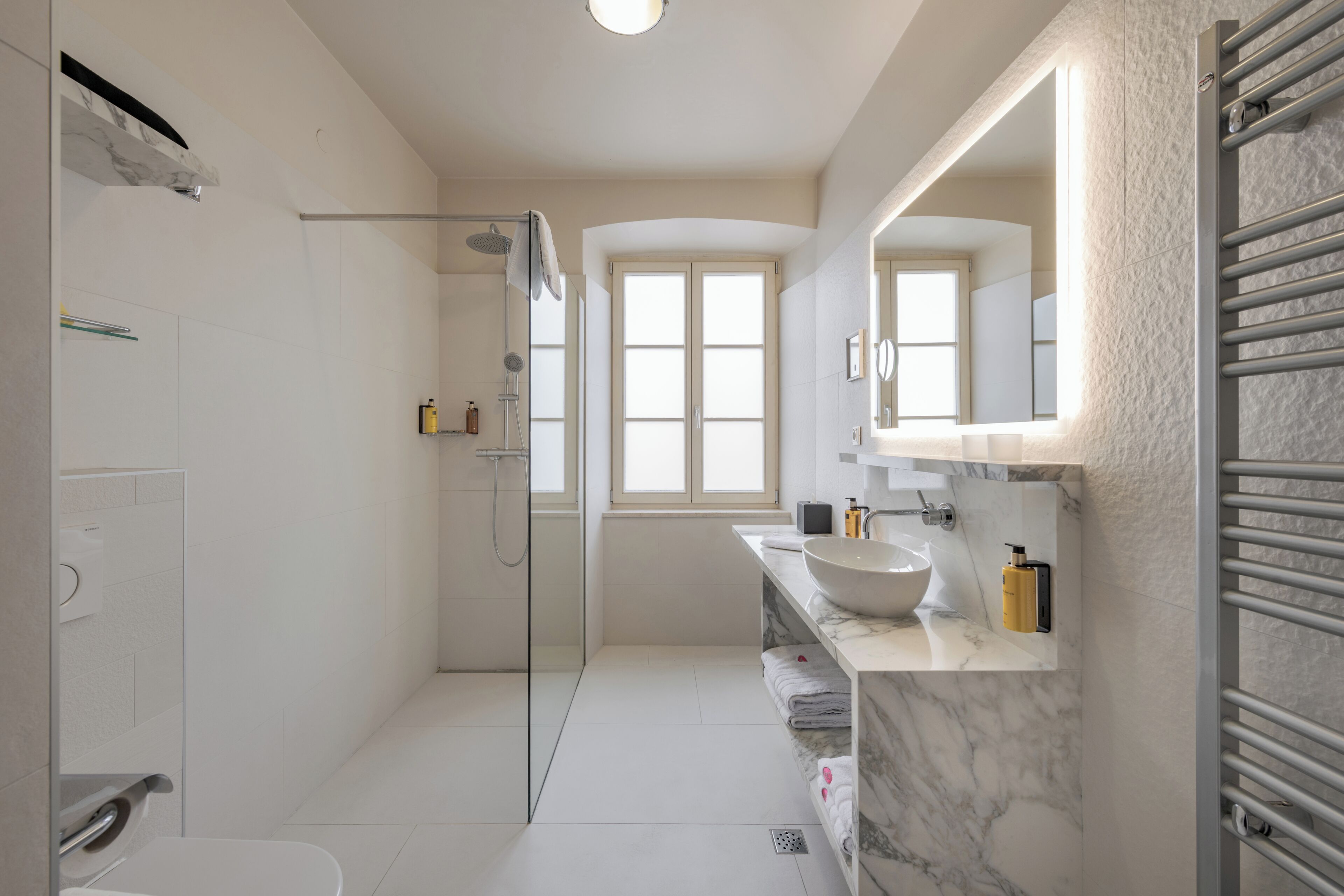 A modern bathroom with a glass shower, a white sink, and a marble countertop.