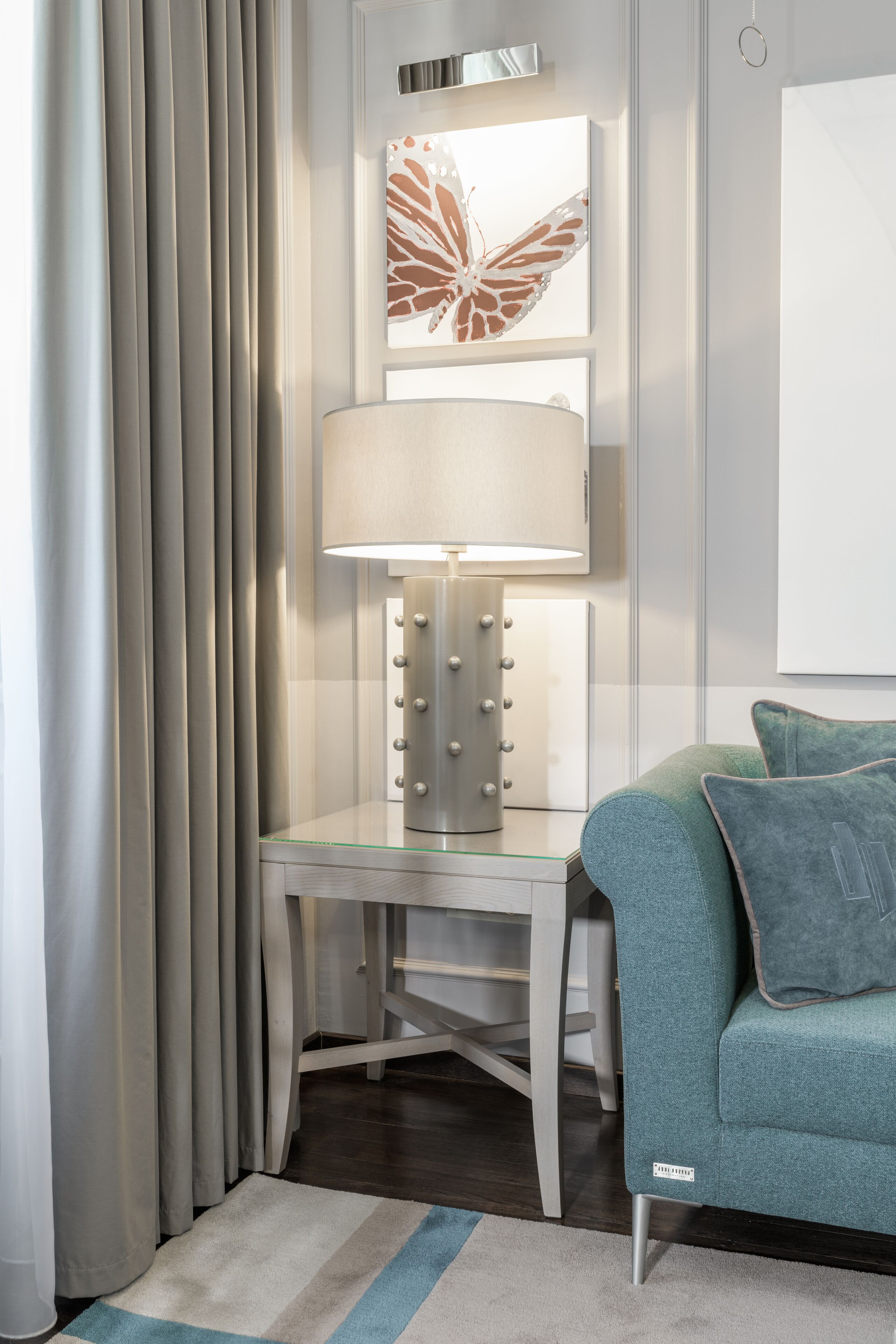 Habitació d'hotel moderna amb un sofà verd mar, una làmpada sobre una taula de vidre i una obra d'art amb forma de papallona a la paret.