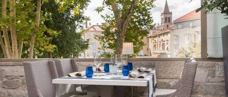 An outdoor dining area with wicker chairs and a table set for four, overlooking a historic building with a tower.