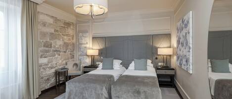 Habitación de hotel con una pared de acento de piedra, dos camas con ropa de cama gris, una araña y una obra de arte grande en la pared.