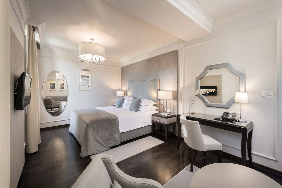 Ein modernes Hotelzimmer mit Bett, Schreibtisch, Stuhl und einem großen Spiegel.