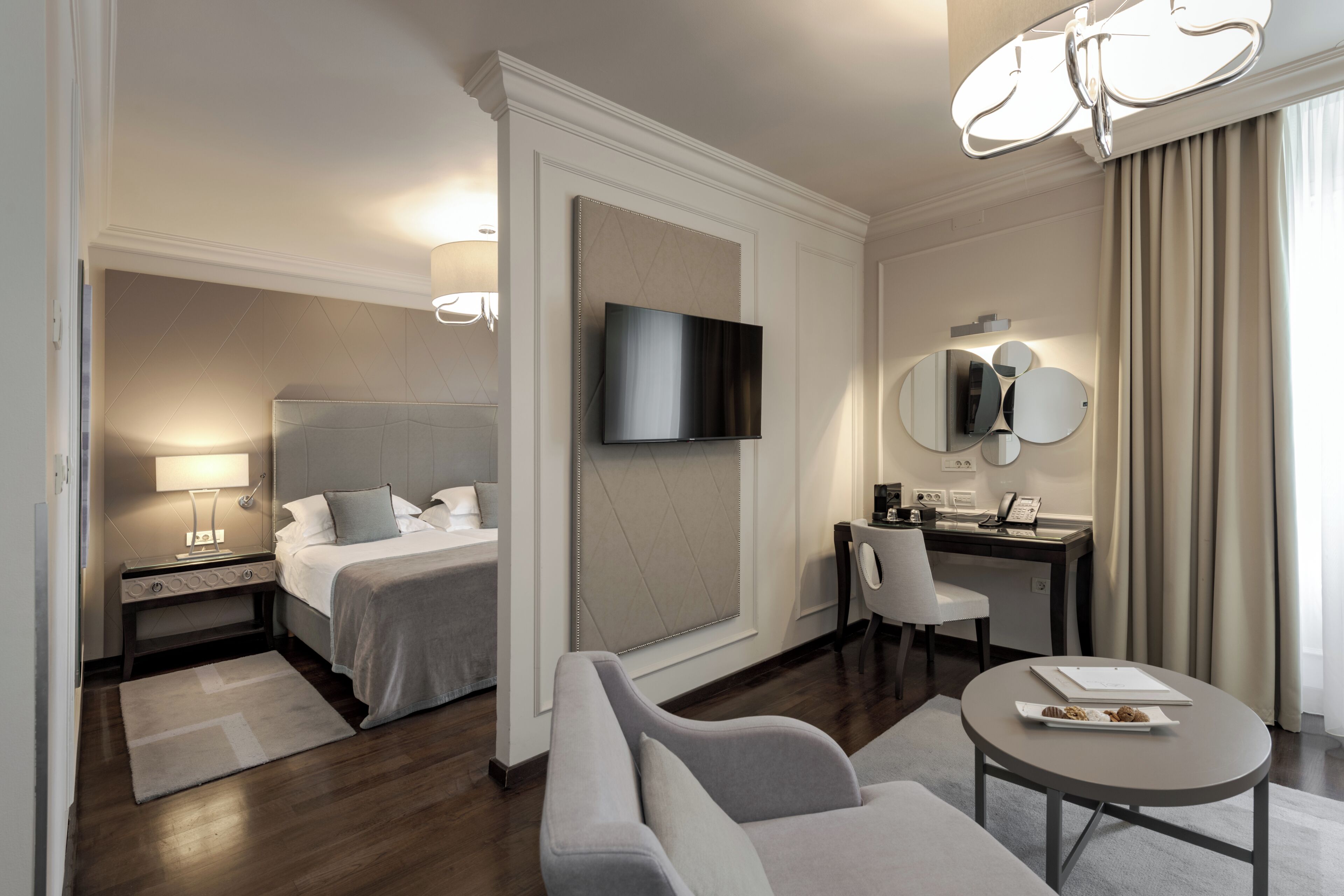 A hotel room with a bed, a sofa, a desk, a chair, a TV, and a dining table with a plate.