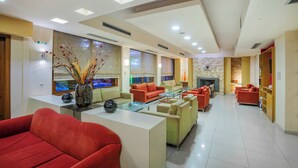 A modern hotel lobby with a fireplace, red and beige sofas, and a decorative vase. - Pefka Hotel (Pylaia-Chortiatis)