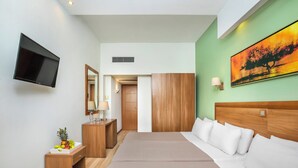A modern hotel room with a large bed, wooden wardrobe, a flat-screen TV, a fruit bowl, and a painting on the wall. - Pefka Hotel (Pylaia-Chortiatis)