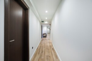 Un pasillo con piso de madera, paredes blancas y una puerta de madera oscura.