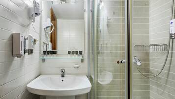 Un baño moderno con ducha envuelta en vidrio, lavamanos blanco y varios artículos de aseo en un estante.