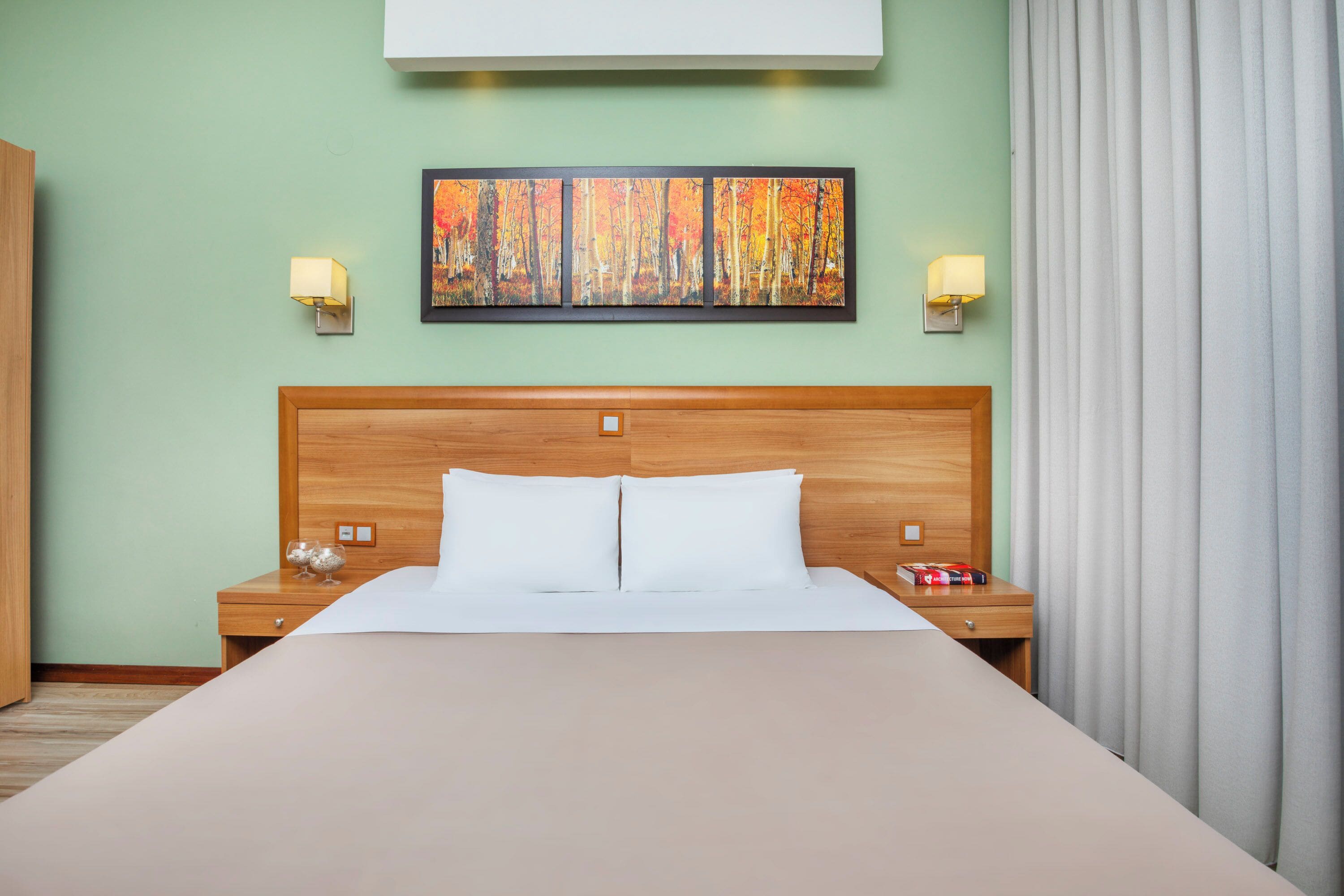 Een hotelkamer met een groot bed, een houten hoofdbord, twee nachtkastjes met lampen en een schilderij in een lijst aan de muur.
