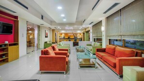 A modern hotel lobby with red and green sofas, a flat-screen TV, and a reception desk. - Pefka Hotel (Pylaia-Chortiatis)