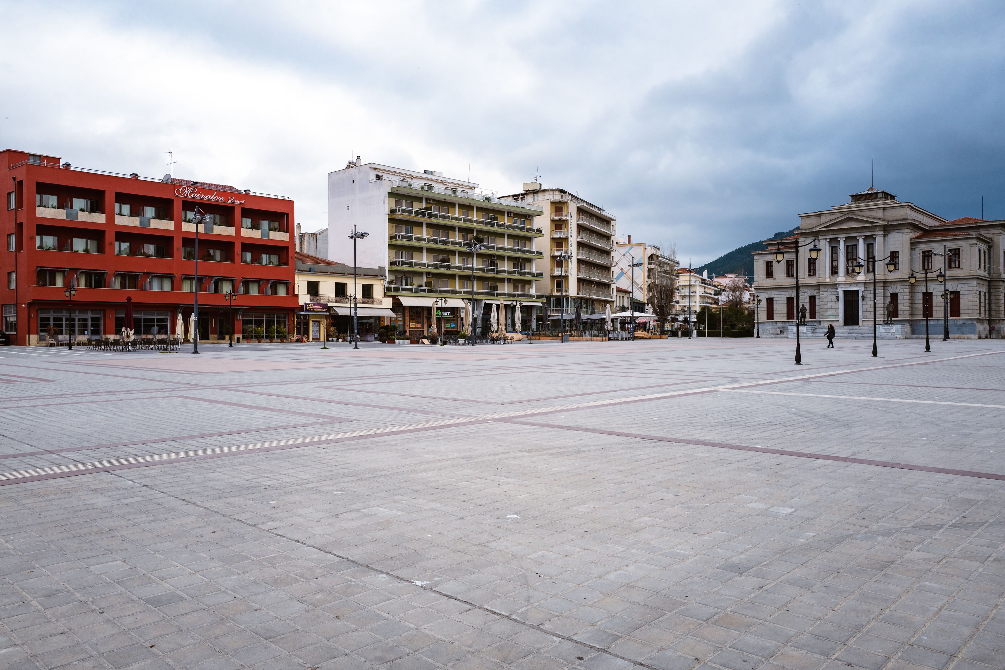 A spacious public square with a red building labeled "Kumelion" on the left, a multi-story building in the center, and a classical building on the right.