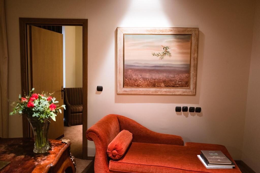 A room with a wooden door, a red sofa, a vase with flowers, and a framed painting on the wall.