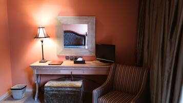Habitación de hotel con escritorio de madera, una computadora, lámpara, silla y un pequeño otoman.