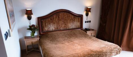A neatly made bed with a brown headboard and footboard, flanked by two bedside tables with lamps, in a room with a carpeted floor.