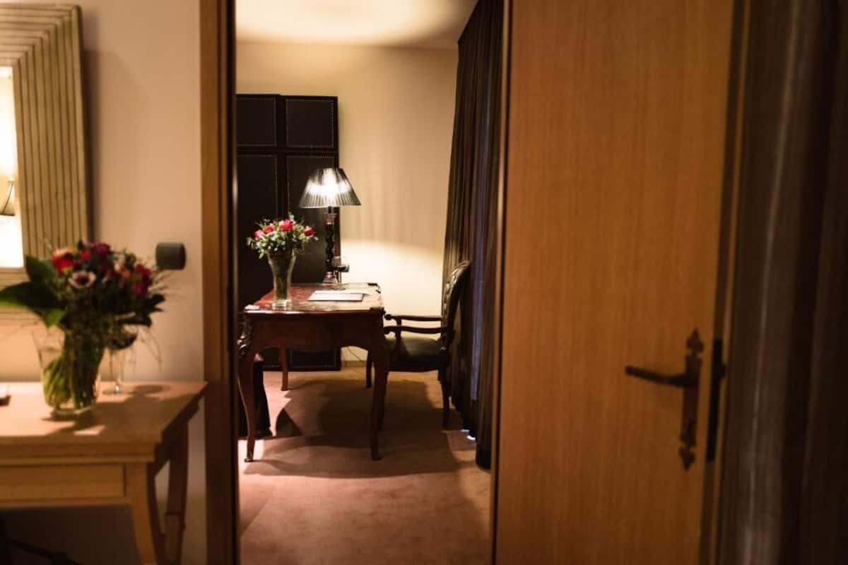 Ein Hotelzimmer mit Holztür, Schreibtisch mit Lampe, Blumenvase und Stuhl.