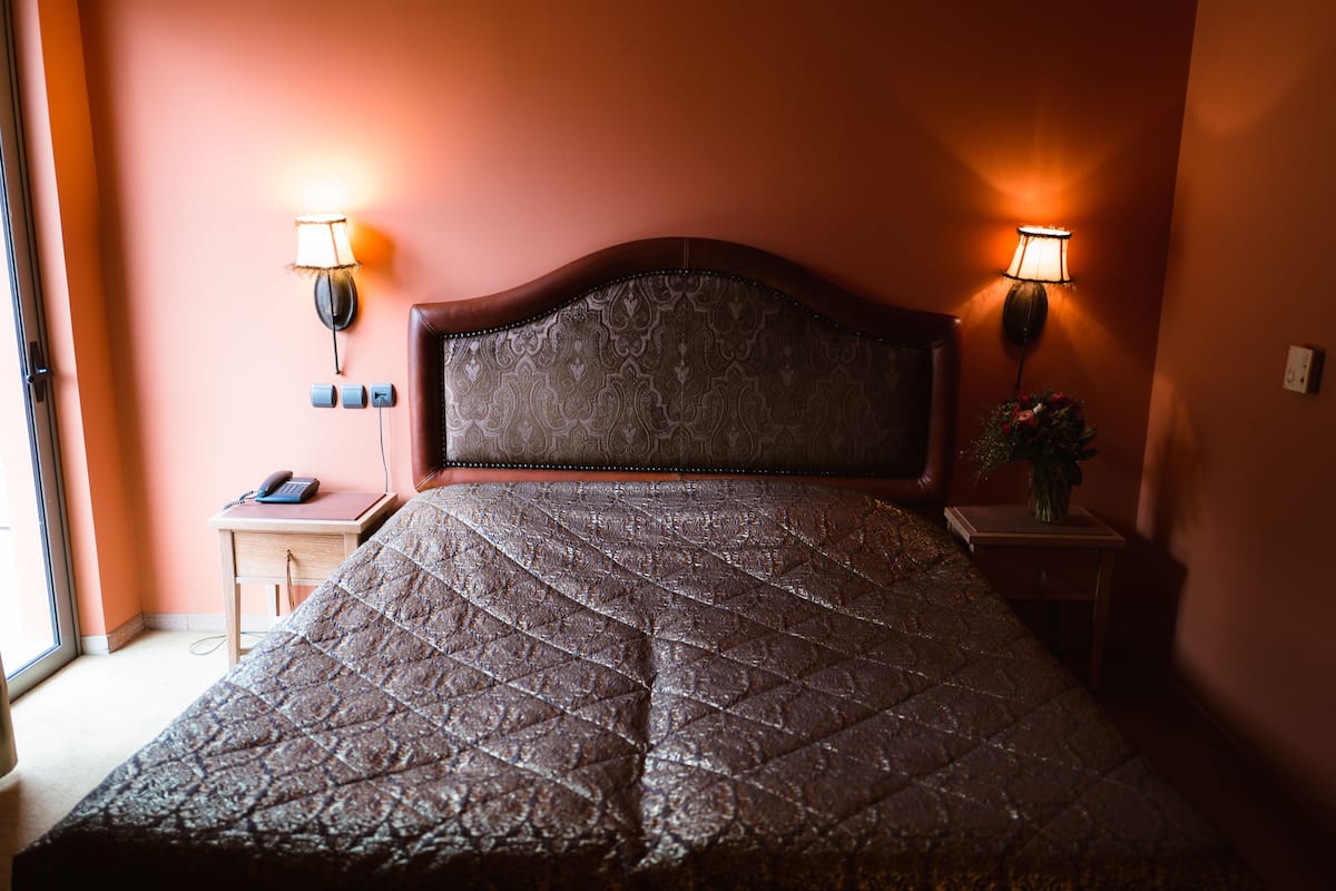 Ein Bett mit gestepptem Kopfteil, zwei Nachttischlampen, ein Nachttisch mit Telefon und ein kleiner Tisch mit Blumenvase.
