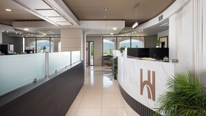 A modern hotel reception area with a glass partition, a reception desk, and a view of the outdoors. - Heaven Hotel (Thermi)