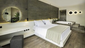 A modern bedroom with a large bed, a built-in bench, a vanity with a mirror, and a bathtub. - Heaven Hotel (Thermi)