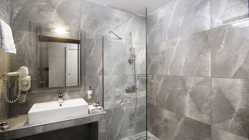 A modern bathroom with a glass-enclosed shower, a white sink, and a marble-tiled wall.