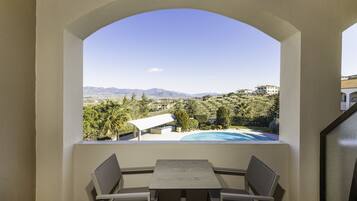 Un balcón con mesa y sillas, con vistas a una piscina y un paisaje montañoso.
