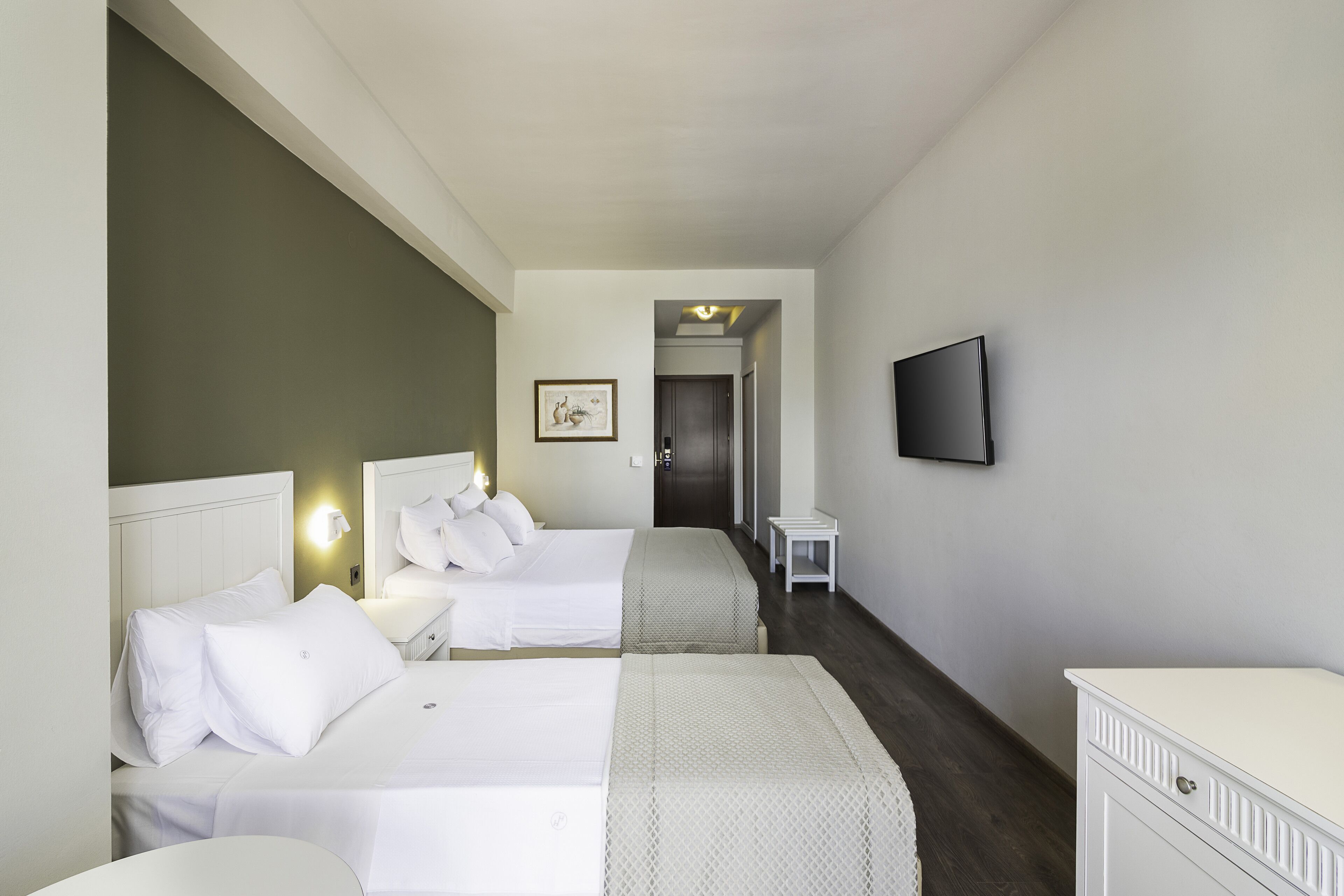 Habitación de hotel con dos camas, un televisor montado en la pared y una mesita de noche pequeña.