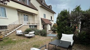 A house with a patio area featuring outdoor furniture, a staircase leading to the entrance, and a garden with various plants.