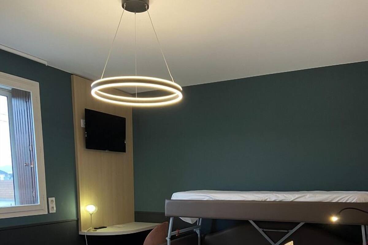 Une chambre d’hôtel avec un lit superposé, un bureau avec une chaise, un téléviseur fixé au mur et un luminaire circulaire au plafond.