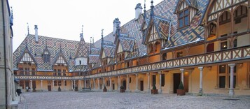 Un patio con suelo adoquinado, una fuente en el centro y edificios con estructura de madera y tejados decorados.