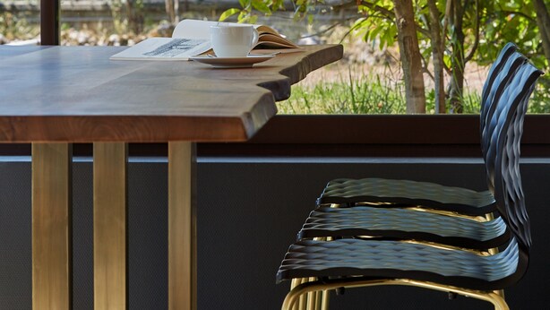 A table with a book and a cup, a chair, and a view of a tree through a window.